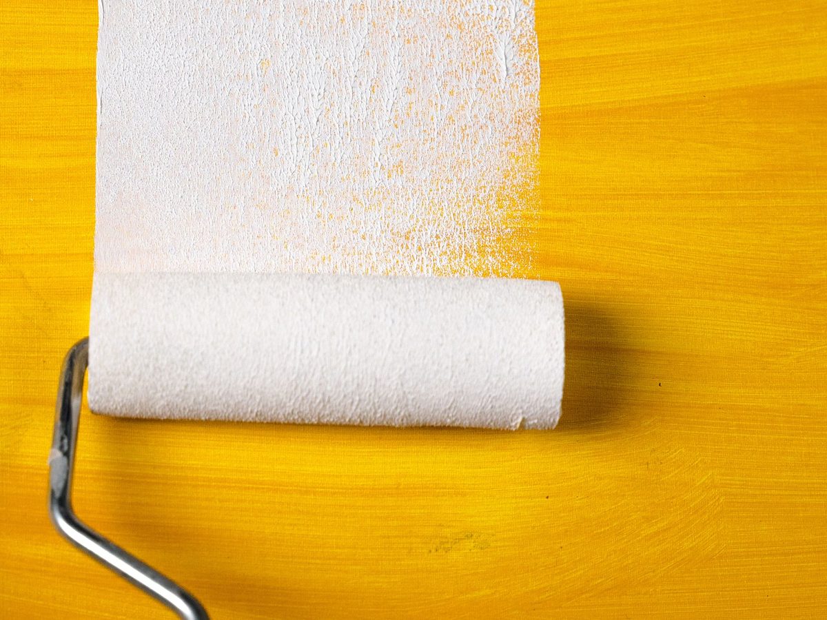 Representative photo: a paint roller laying a fresh white stripe over a yellow surface